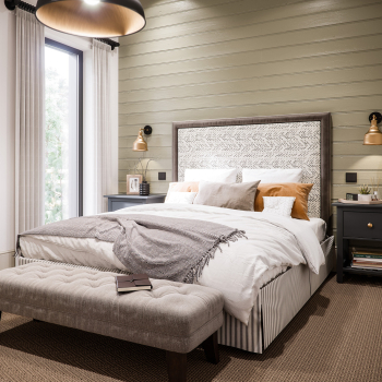 Architectural CGI interior - A neatly arranged bedroom featuring a large bed with white and tan bedding, framed artwork above a wood-paneled wall, and a reading nook by the window with a small desk and chair. There's ambient lighting from wall-mounted lamps.